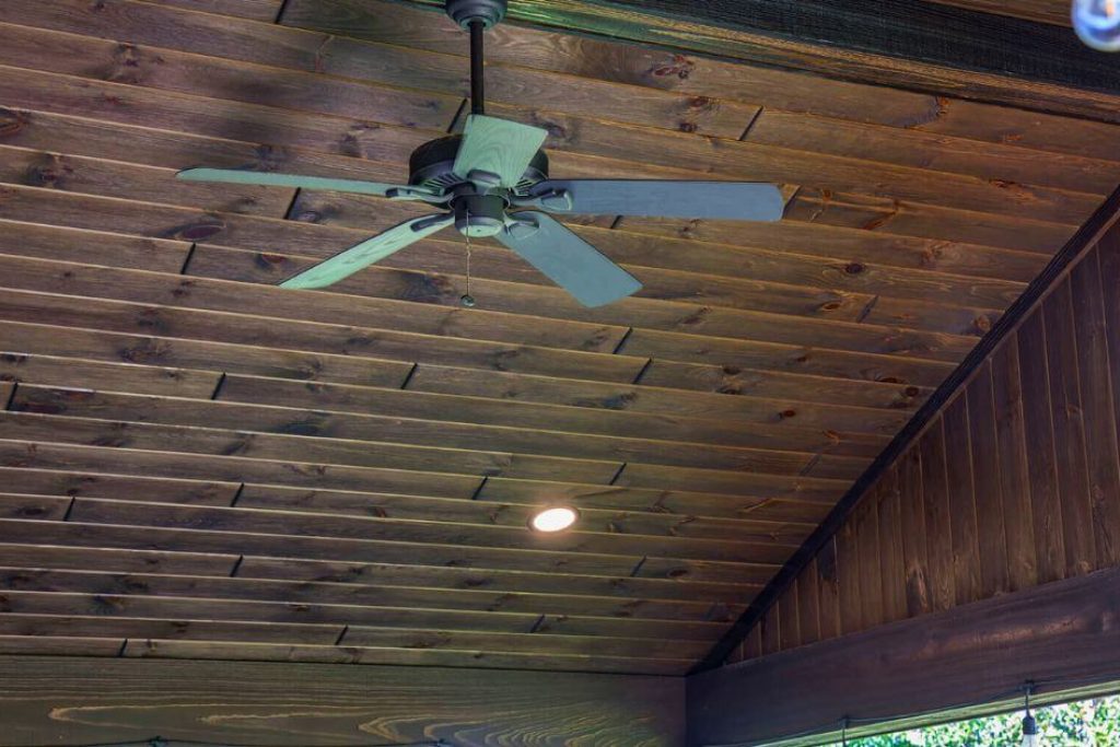 dark brown wood ceiling planks over a porch with a black outdoor fan