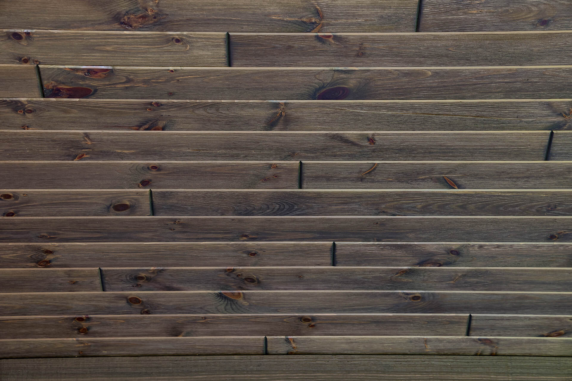 Close-up view of dark-stained wood wall planks with visible knots and grain, illustrating one of the best wood choices for walls in rustic or modern interiors.
