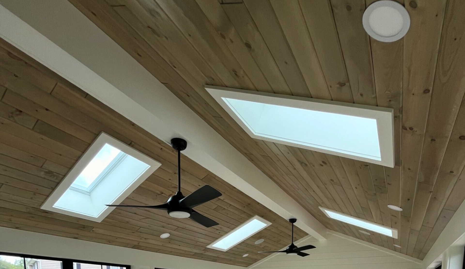 Wood ceiling living room with natural planks, skylights, and black ceiling fans