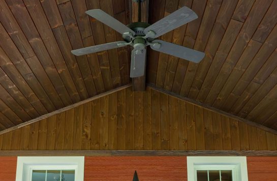 vintage brown wood ceiling on porch with ceiling fan and red siding wall