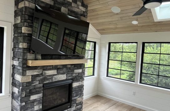 modern sunroom with stone fireplace, ceiling fan, and prefinished wood paneling