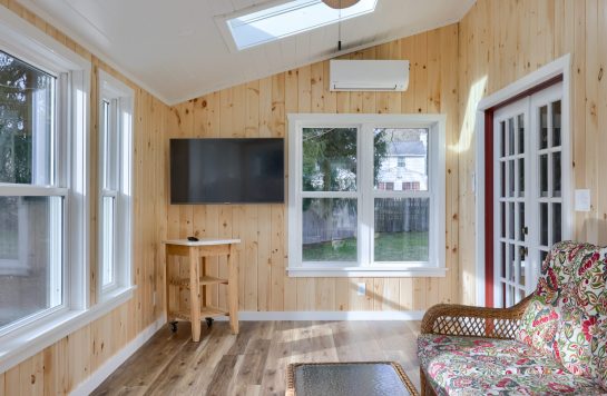 sunroom living space with prefinished wood paneling walls, television, and wicker furniture