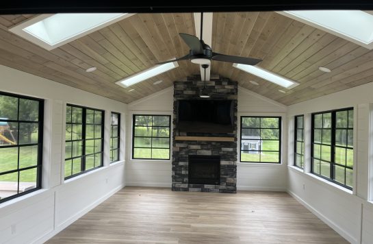 modern sunroom ceiling finished in wood paneling with skylights and stone fireplace