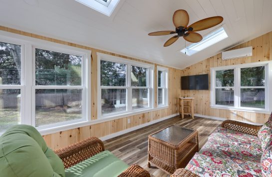 sunroom interior featuring prefinished wood paneling on walls with wicker seating and ceiling fan