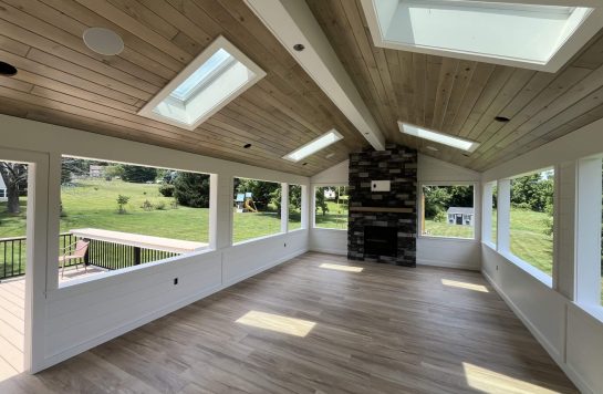 large sunroom with skylights, stone fireplace, and ceiling finished in wood paneling